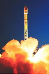 Rocket rising at night above bright orange flames and exhaust.