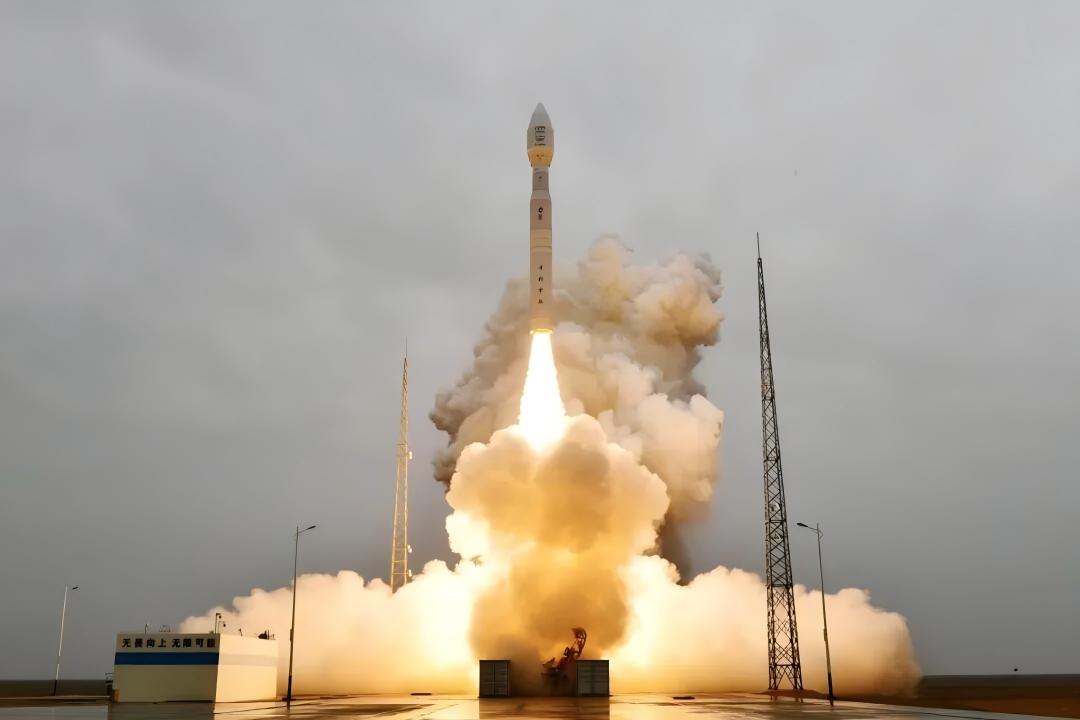 Rocket leaving a launch pad amid bright exhaust under an overcast sky.