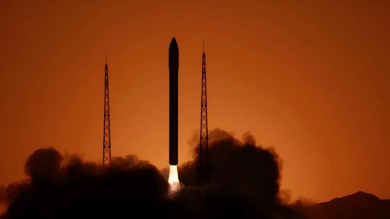 Rocket lifting off against an orange-lit sky with dark exhaust clouds below.