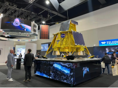 Gold-foil-covered spacecraft model on a raised platform inside an exhibition hall.