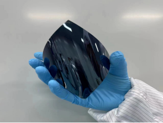 A blue-gloved hand bending a dark flexible photovoltaic sheet.