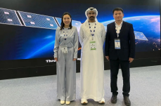 Three visitors posing in front of a spacecraft and solar-array display backdrop.